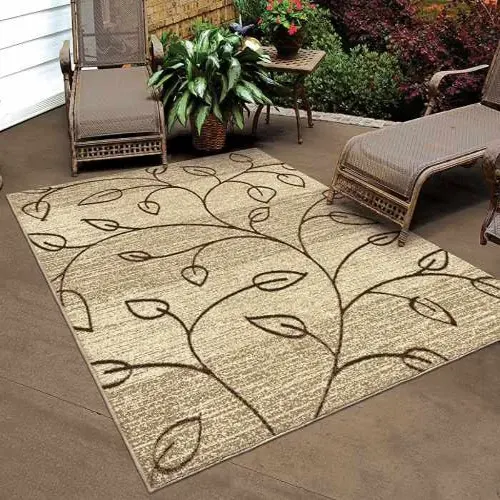 A beige outdoor rug with a brown leaf pattern, placed on a concrete patio between two outdoor lounge chairs