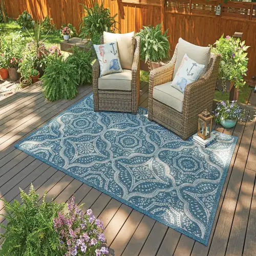 A blue and white outdoor rug with an intricate pattern is placed on a wooden deck