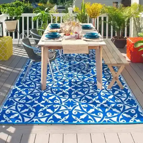 A blue and white patterned outdoor rug placed under a wooden dining table and chairs on a deck