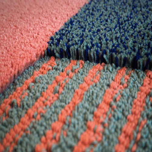 A close-up of a colorful wool rug with geometric patterns in shades of pink, blue, and gray