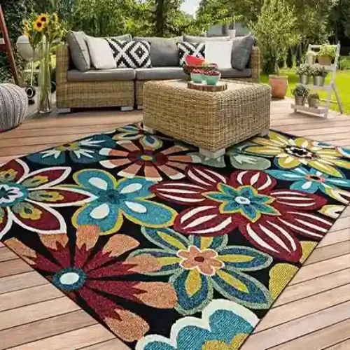 A colorful floral outdoor rug with red, blue, yellow, and green flowers, placed on a wooden deck