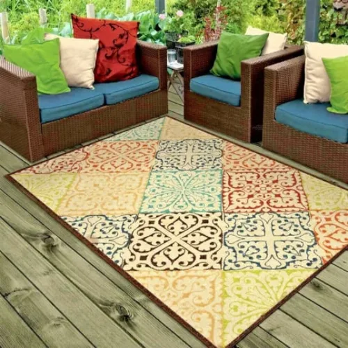 A colorful outdoor rug with a patchwork pattern, placed on a wooden deck