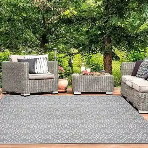 A gray outdoor rug with a geometric pattern is placed on a wooden deck