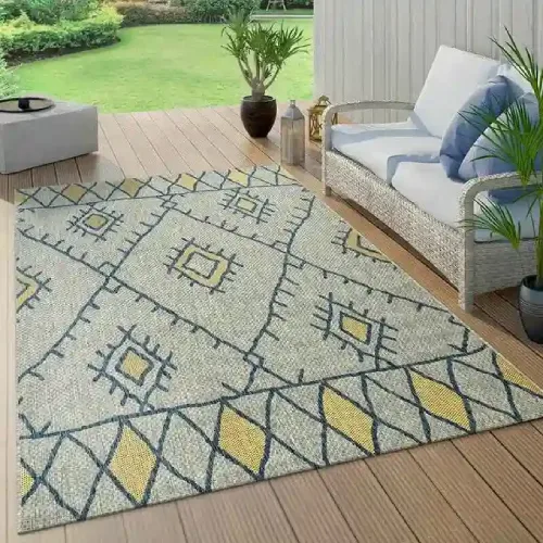 A gray outdoor rug with a yellow geometric pattern, placed on a wooden deck in front of a wicker sofa