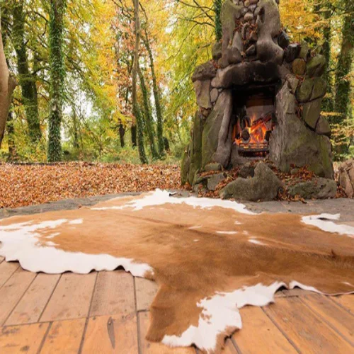 A large animal skin rugs placed in front of a stone fireplace in a rustic outdoor setting