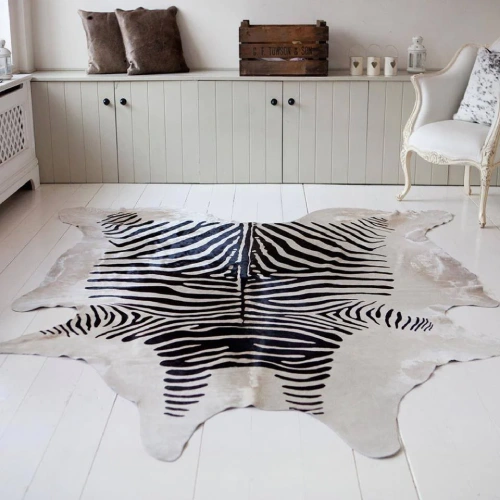 A large, black and white animal skin rugs is laid out on a white wooden floor