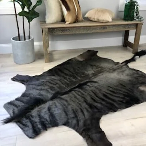 A large, dark brown wildebeest hide rug is laid out on a wooden floor