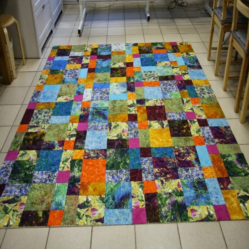 A large patchwork quilt displayed on the floor in a workshop setting