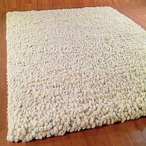 A luxurious, cream-colored wool rug with a textured, pebble-like surface