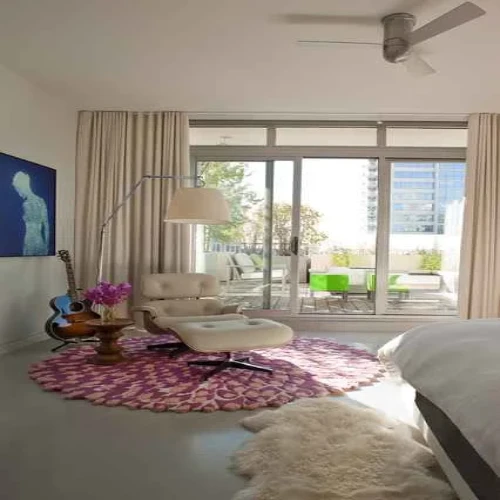 A modern bedroom in Dubai featuring a round rug with a floral pattern, a white armchair, a floor lamp, and a ceiling fan