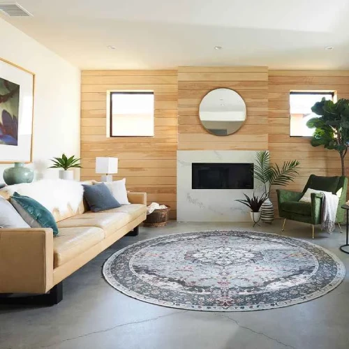 A modern living room featuring a round rug in Dubai, with a brown leather sofa, a marble fireplace