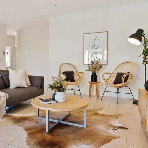 A modern living room with a gray sofa, two rattan armchairs, and a round wooden coffee table with a cowhide rugs underneath