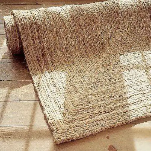 A rolled-up sisal rug with a braided border, partially unfurled on a wooden floor