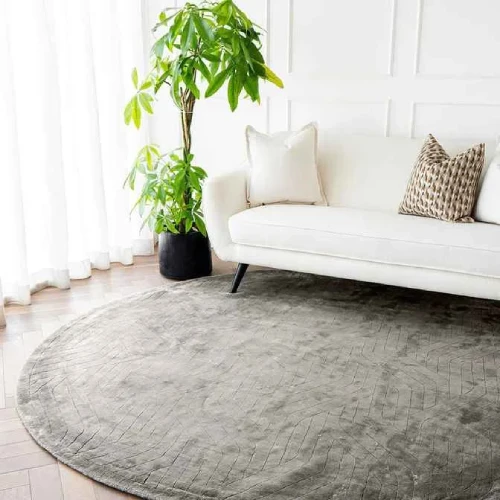 A round rug in a soft gray color with a subtle geometric pattern, placed in a modern living room