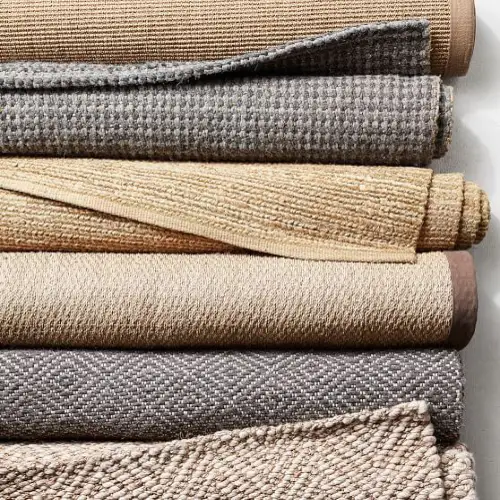 A stack of rolled rugs in various neutral colors, including beige, brown, and gray