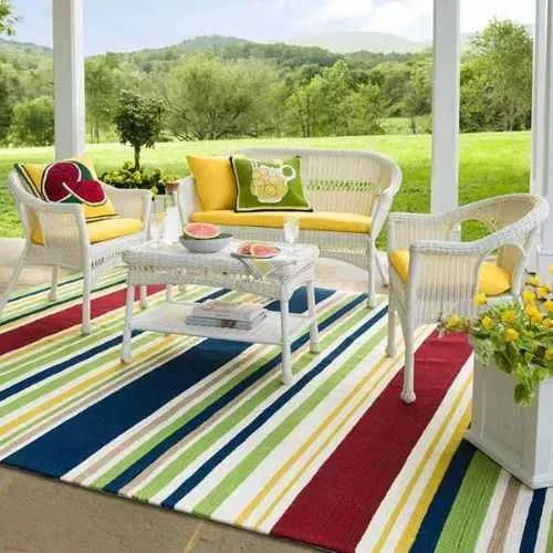 A white wicker patio furniture set with colorful striped outdoor area rug