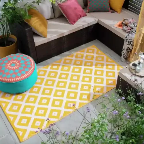 A yellow and white outdoor rug with a geometric pattern is placed on a patio