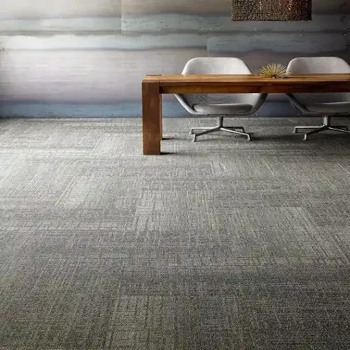 Modern office space with a gray, textured carpet. A long wooden table and two white chairs