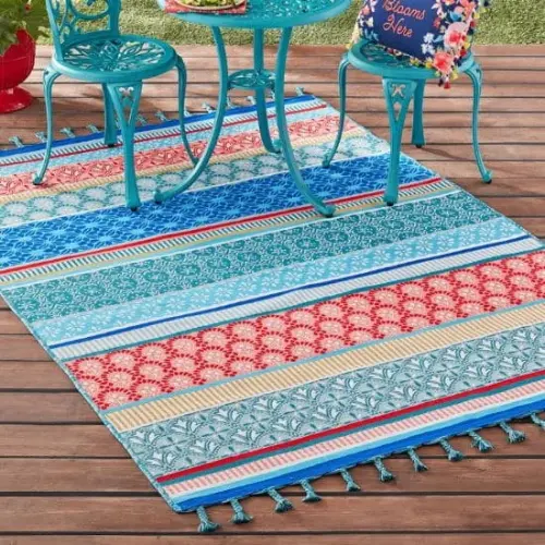 Outdoor rugs with horizontal stripes in red, blue, yellow, and green, placed on a wooden deck