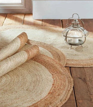 Two round jute rugs with a braided border, one rolled up and the other placed on a wooden floor