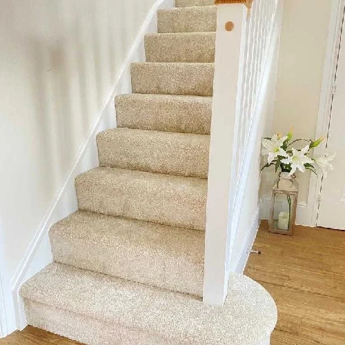 A beige stair carpet on a carpeted staircase with a white railing and a curved landing