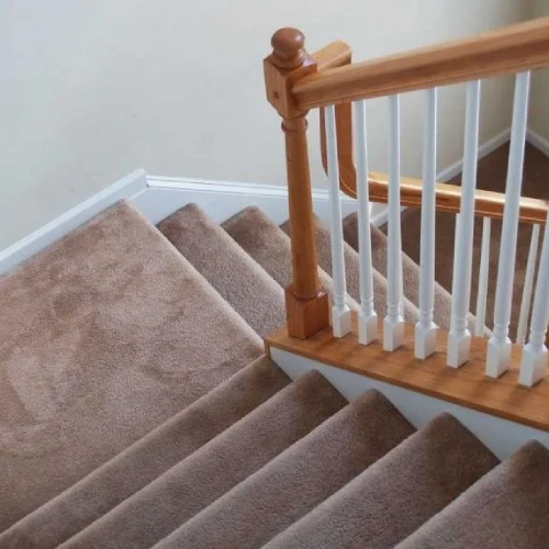 A beige stair carpet on a carpeted staircase with a white railing and a wooden handrail