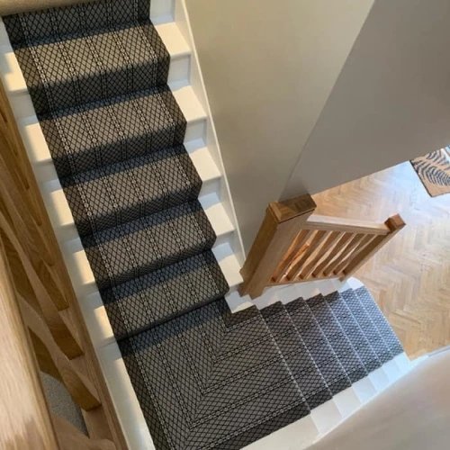 A black and white geometric stair carpet runner is installed on a carpeted staircase with wooden handrails