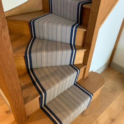 A gray and blue striped stair carpet runner on a wooden staircase with natural wood tones