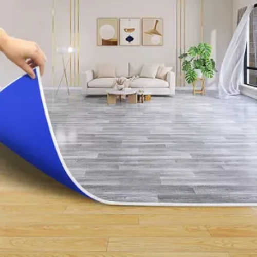 A person unrolling a blue vinyl carpet in a living room